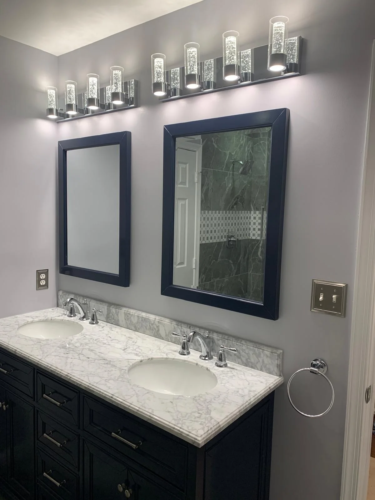Bathroom vanity with dark cabinetry, stone counter, mirrors and lighting