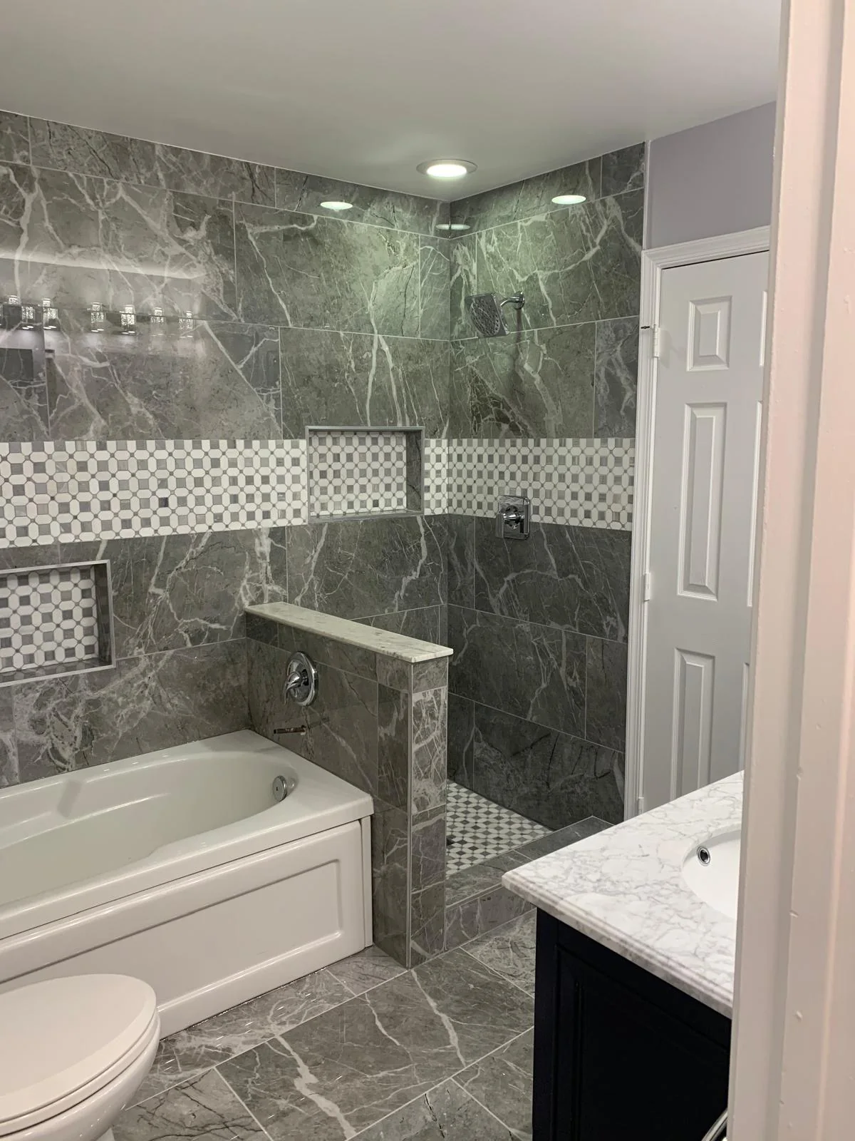 Bathroom with gray wall tile, tub, vanity and updated fixtures