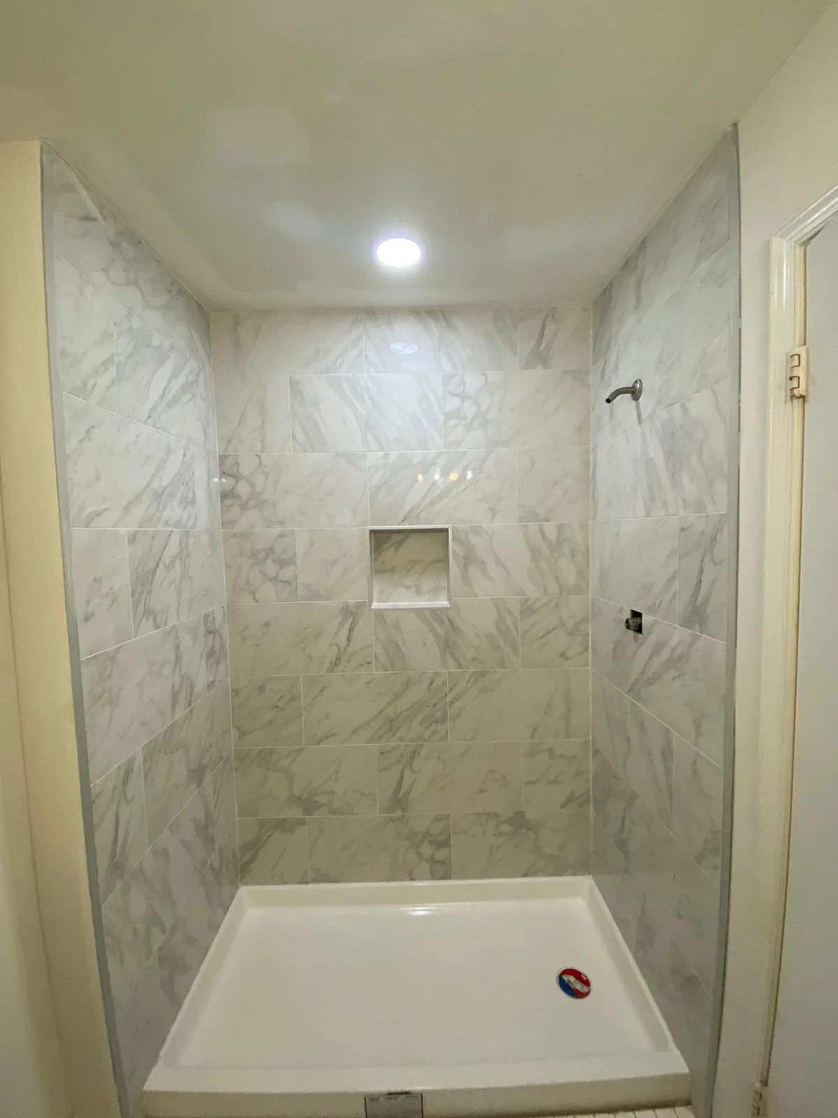 Walk-in shower finished with light marble-look tile and recessed niche