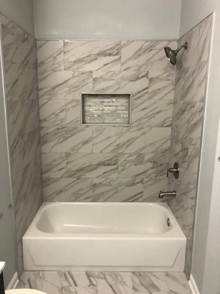 Bathroom tub area with marble-look tile surround and finished fixtures