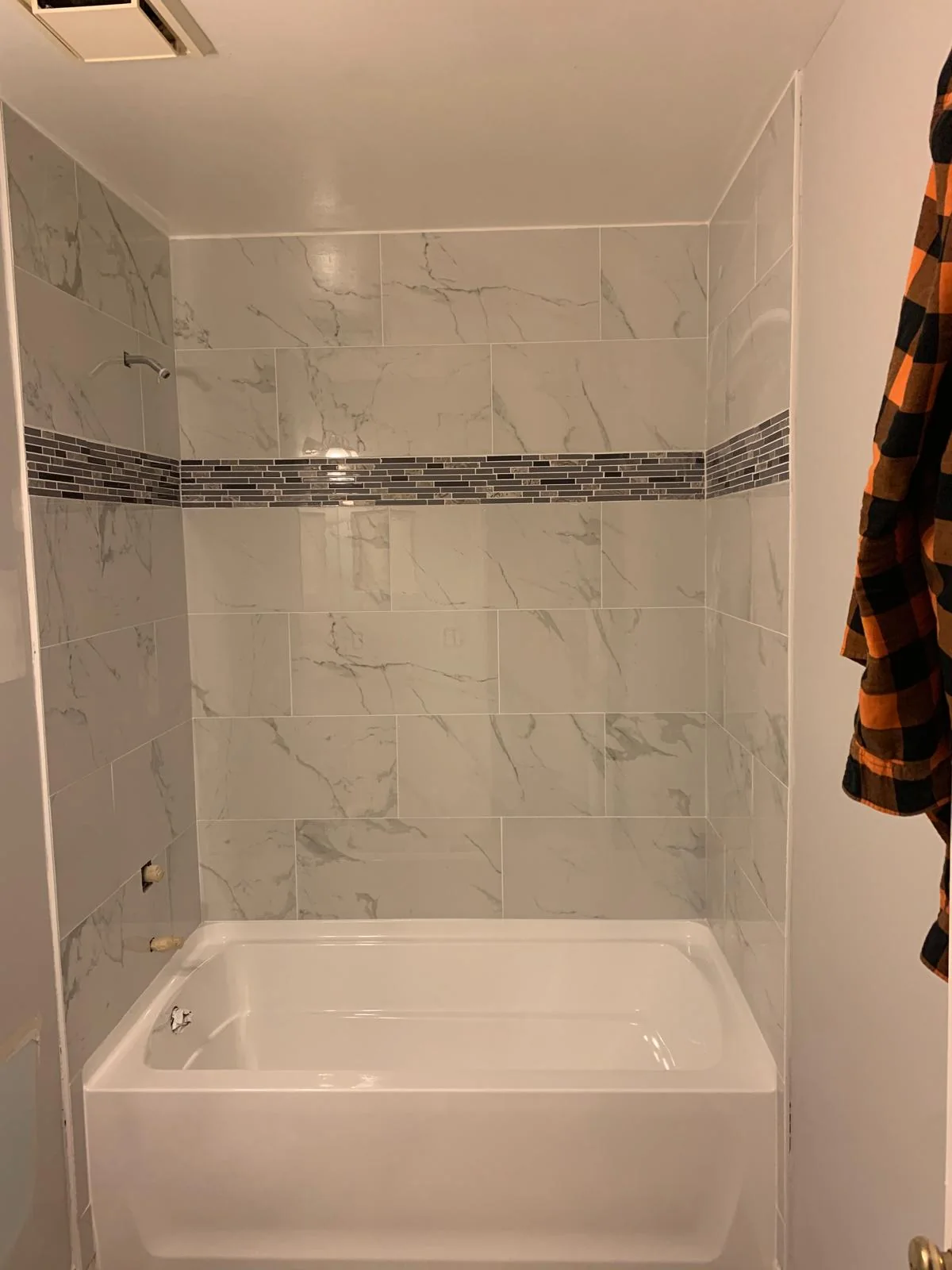 Bathroom tub surround finished with marble-look wall tile and accent band