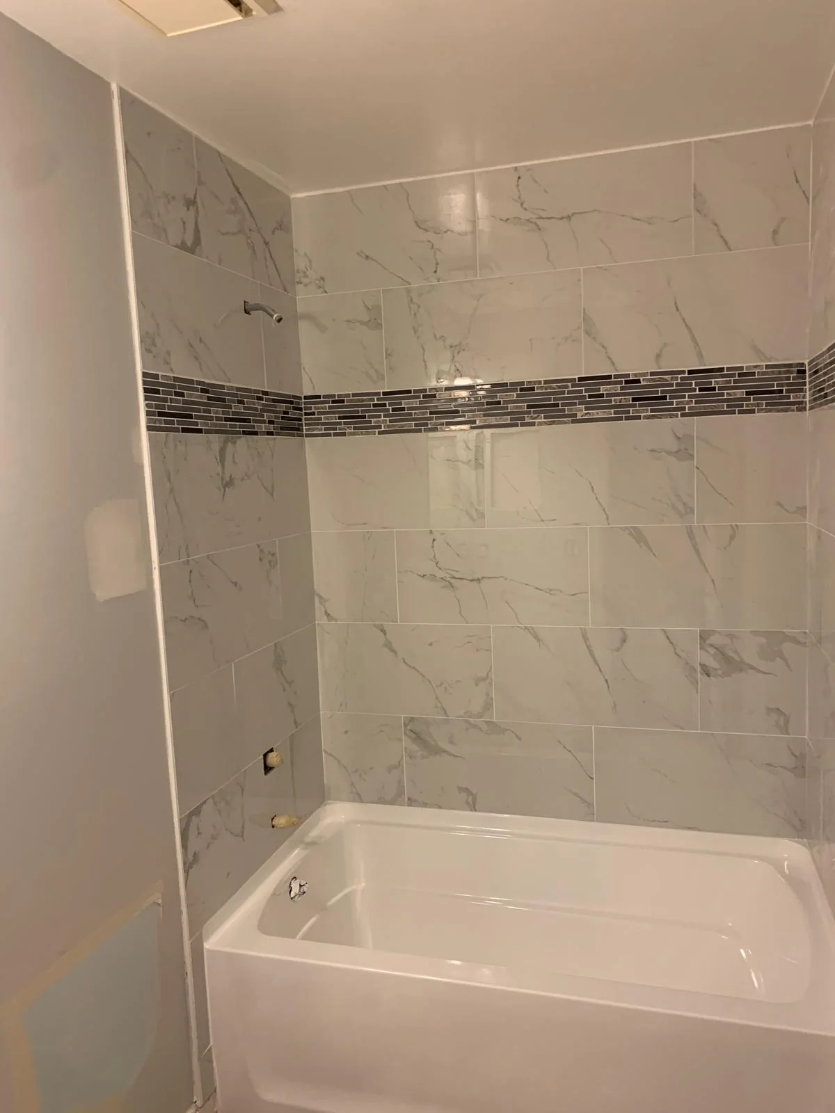 Close view of tiled bathtub surround with marble-look surfaces