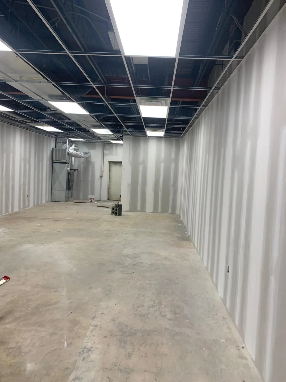 Long commercial corridor during drywall installation and finishing