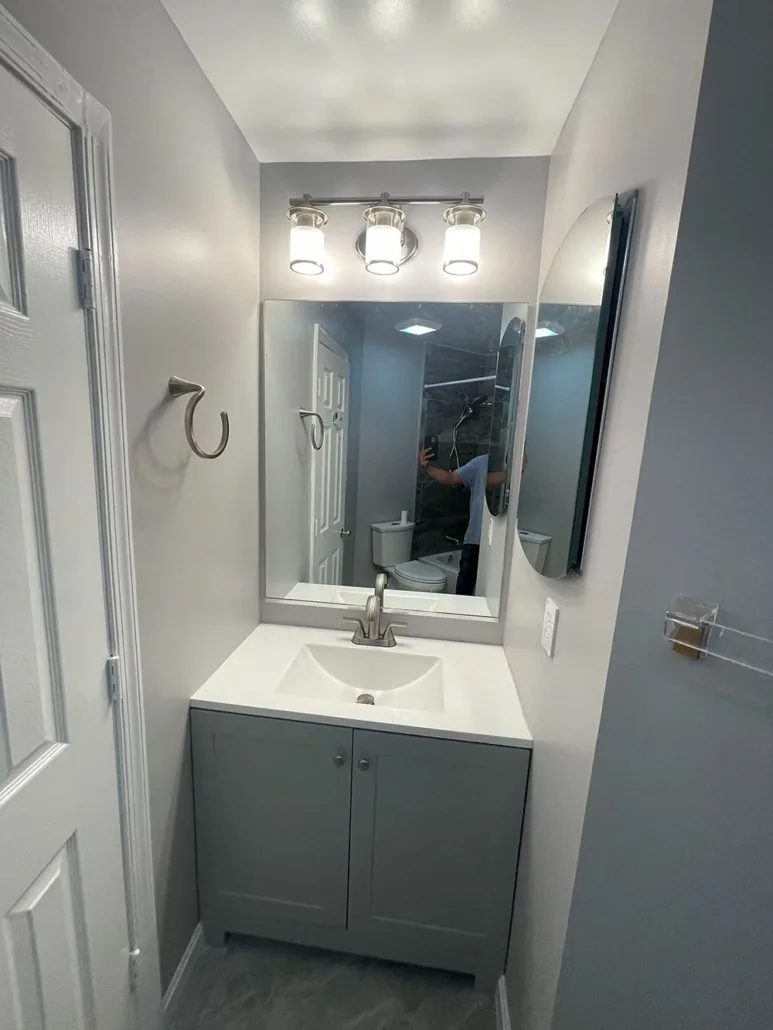 Completed compact bathroom with gray vanity, mirror and lighting