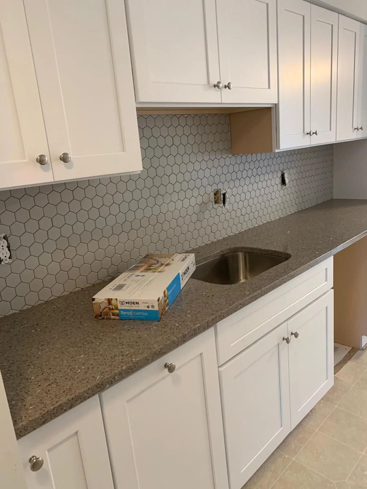 White kitchen sink area with tiled backsplash and stone-look countertop