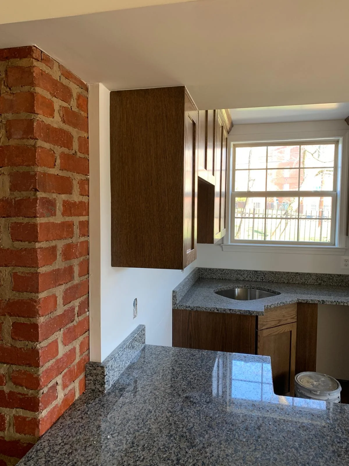 Wood kitchen cabinetry beside exposed brick and stone countertop